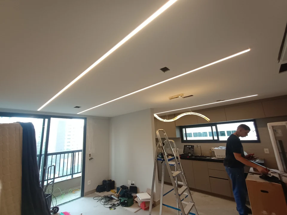 Ambiente em obra com iluminação linear acesa, pendente e profissional trabalhando
